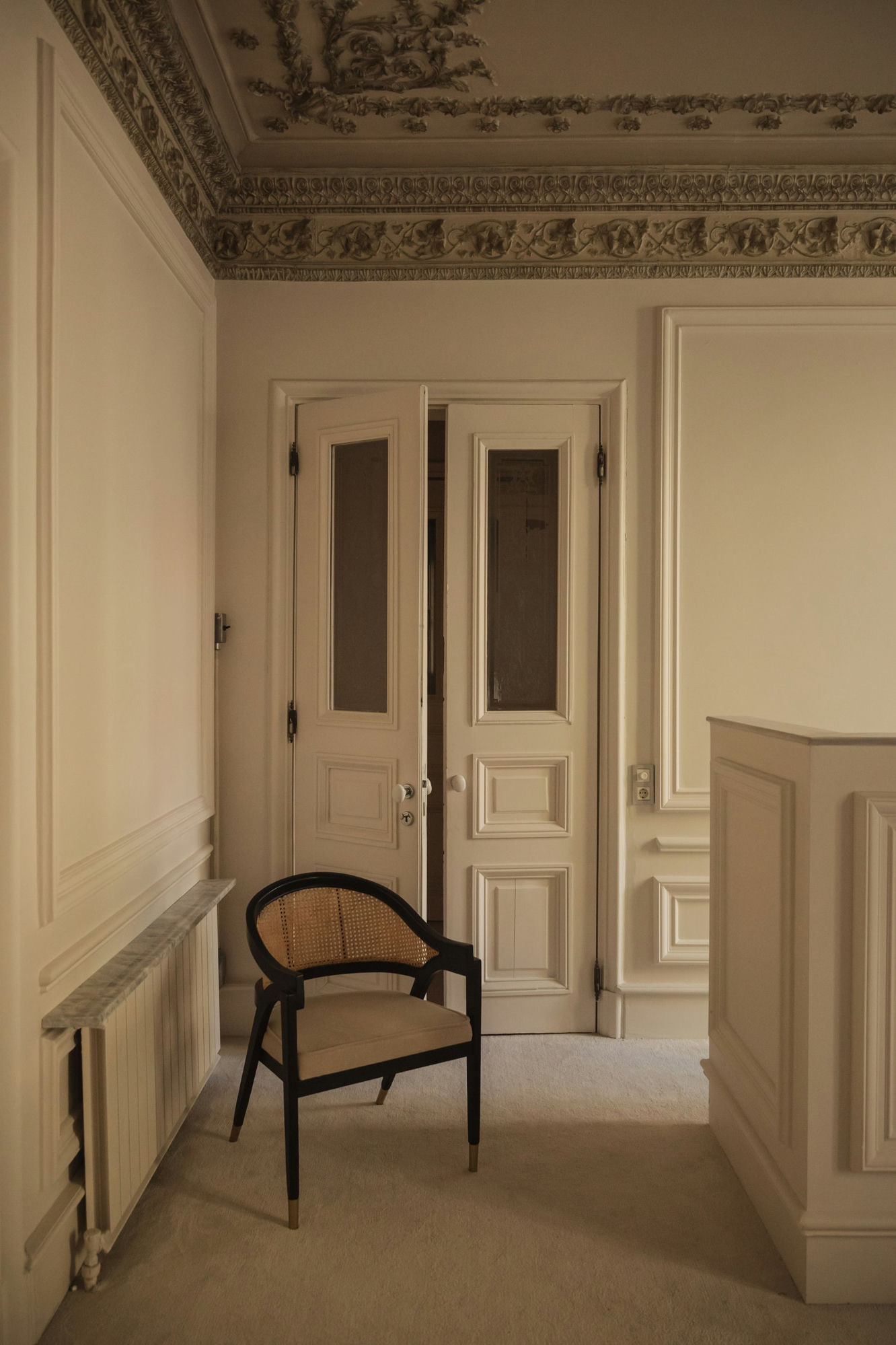 Classical interior with ornate plaster ceiling, paneled doors, and cane chair