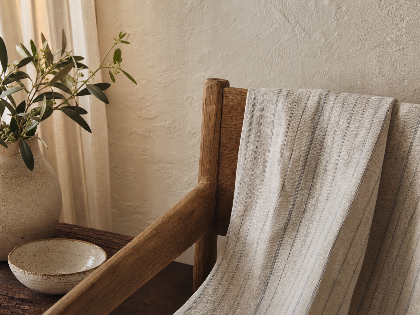 A soft striped linen draped over warm wood beside cream ceramics