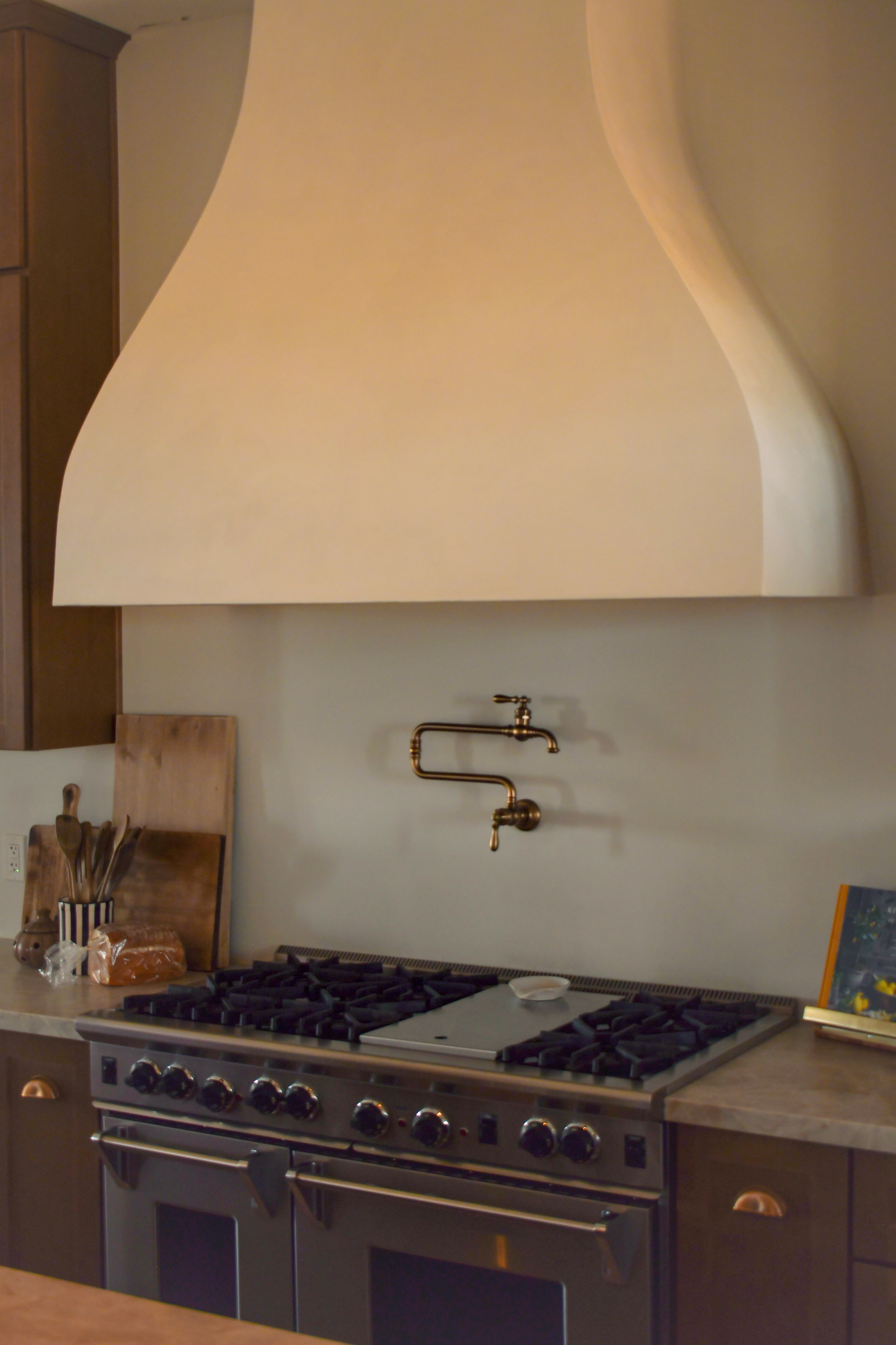 A warm kitchen range, plaster hood, brass pot filler, and wood cooking tools