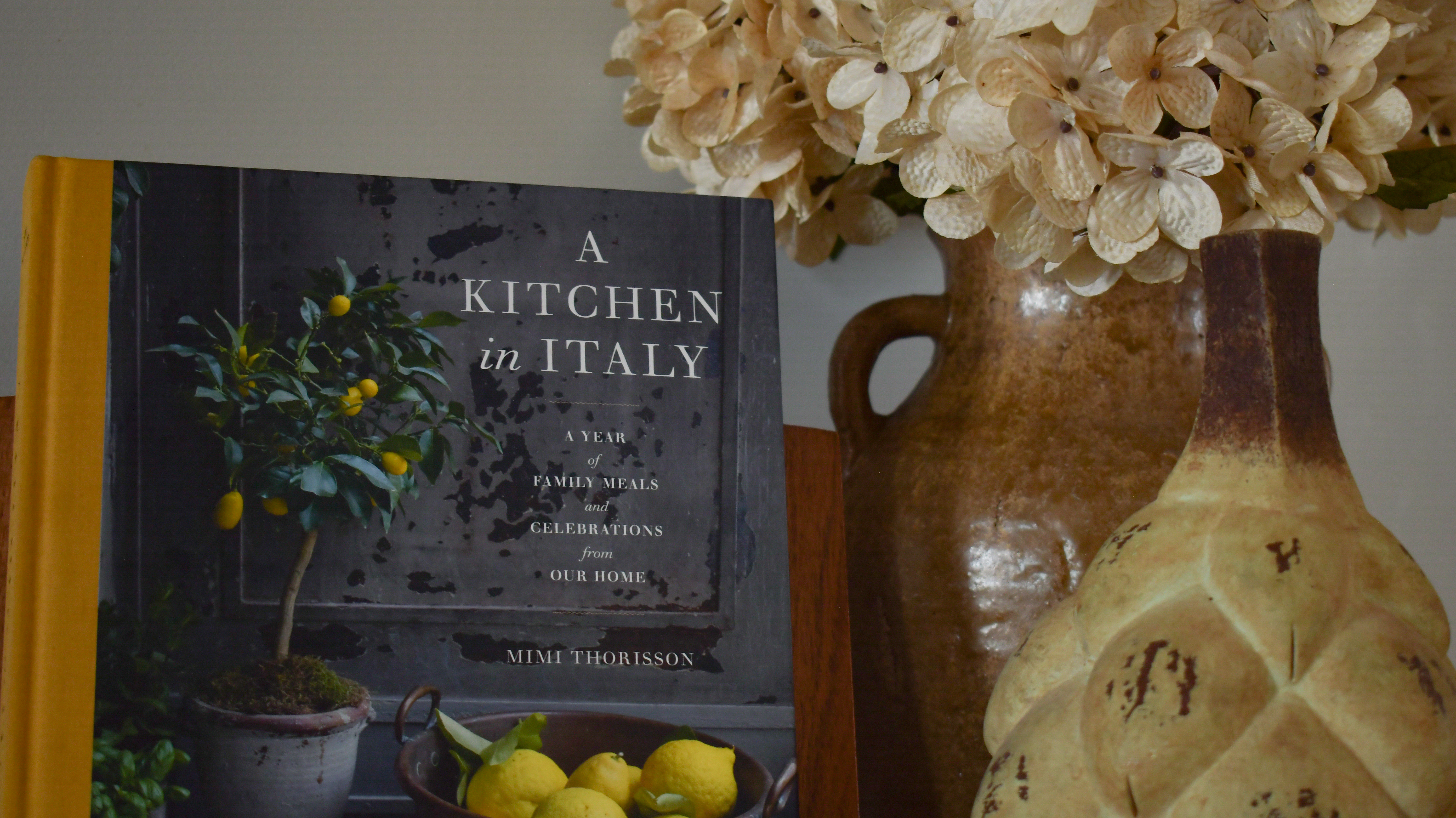 A kitchen book, handmade vessels, preserved flowers, and lemons arranged on a shelf