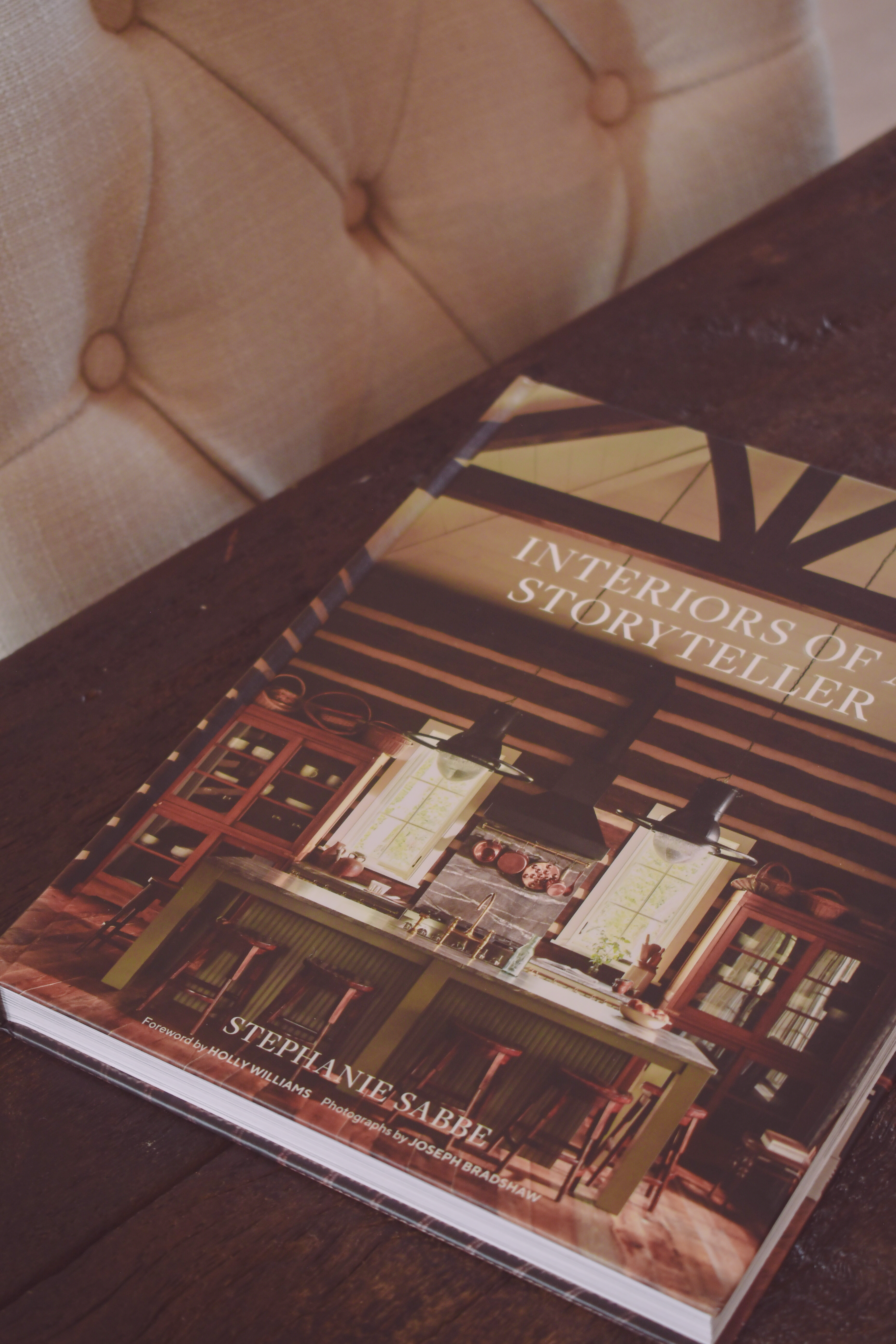 An interiors book resting on a dark table beside a softly tufted chair