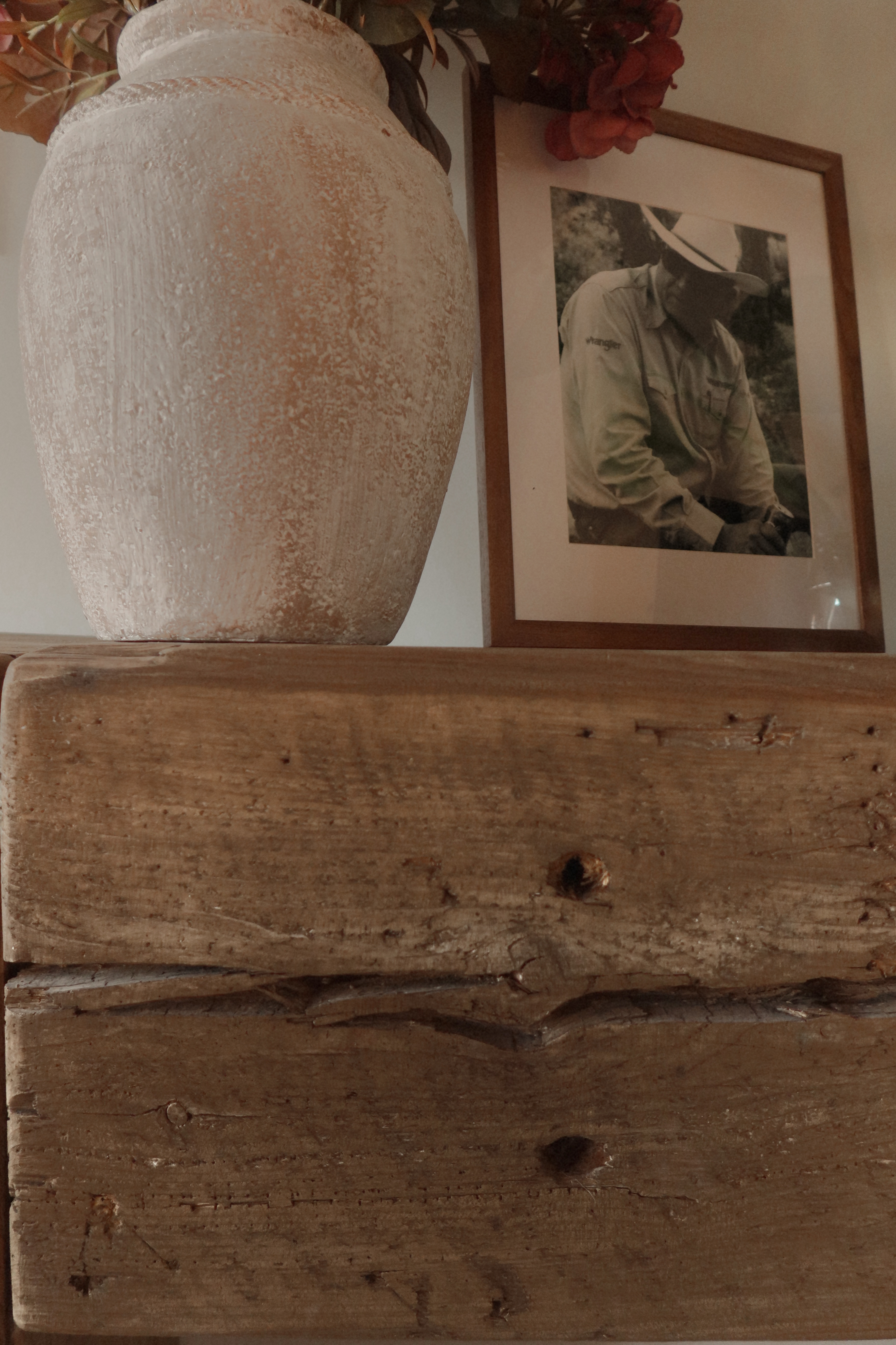 A weathered vase, framed ranch photo, flowers, and old wood mantel detail